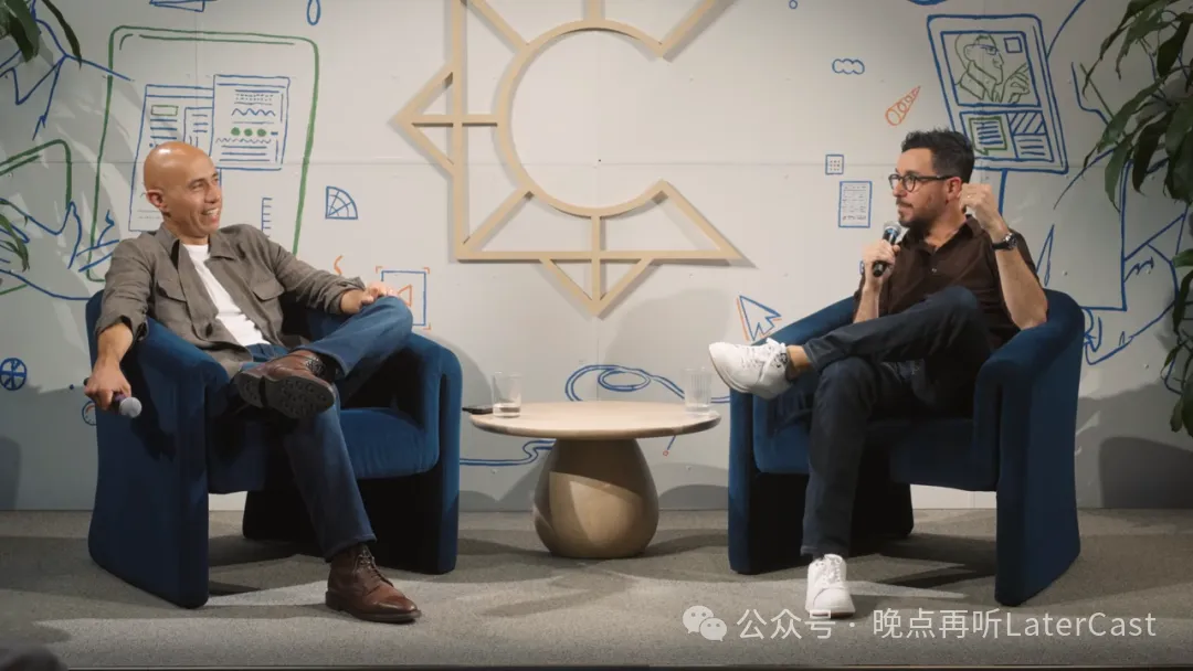 图片展示了两位男士在室内进行对话的场景。左侧男士穿着灰色外套、白色T恤和蓝色牛仔裤,脚穿棕色鞋子,坐在蓝色椅子上,手握麦克风。右侧男士穿着棕色衬衫、黑色裤子和白色运动鞋,同样坐在蓝色椅子上,手握麦克风。背景为白色墙面,上面有蓝色线条图案和几何图形。墙角摆放着绿色植物。图片与上下文关系紧密,可能是记录了Joel Lewenstein向Soleio讲述妻子课程大纲经历的场景。